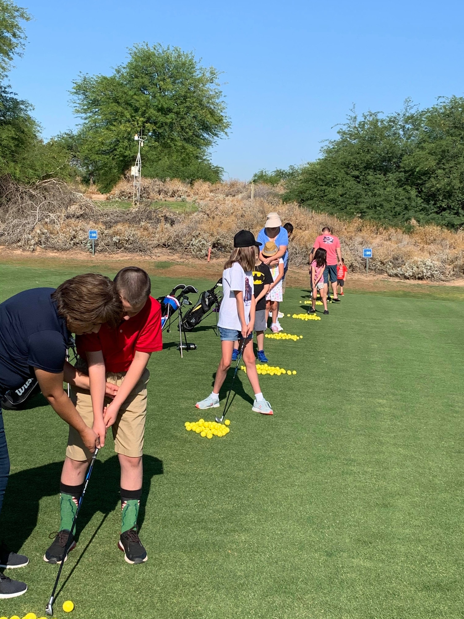 Senaida Larson, far left, 56th Force Support Squadron Airman & Family Readiness Center Exceptional Family Member Program-Family Support coordinator, assists a child with golfing during the Junior Gold Camp July 11, 2021, at Falcon Dunes Golf Course, Luke Air Force Base, Arizona. The Junior Gold Camp gives children an outlet to play sports and engage in a fun activity with EFMP representatives and other children. The EFMP helps support Airmen and their families by providing specialized services to aid in enhancing their quality of life and level of resiliency. (Courtesy photo)