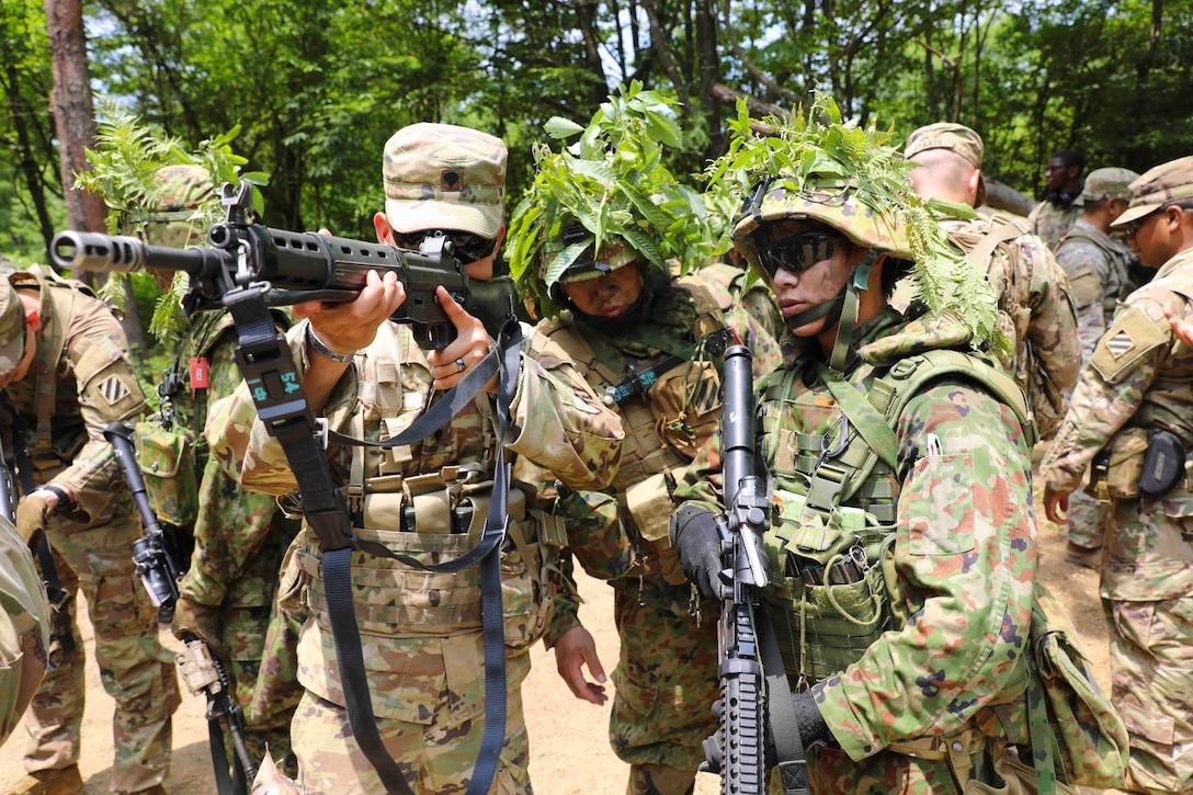 A soldier looks through the scope of a weapon as others stand around.