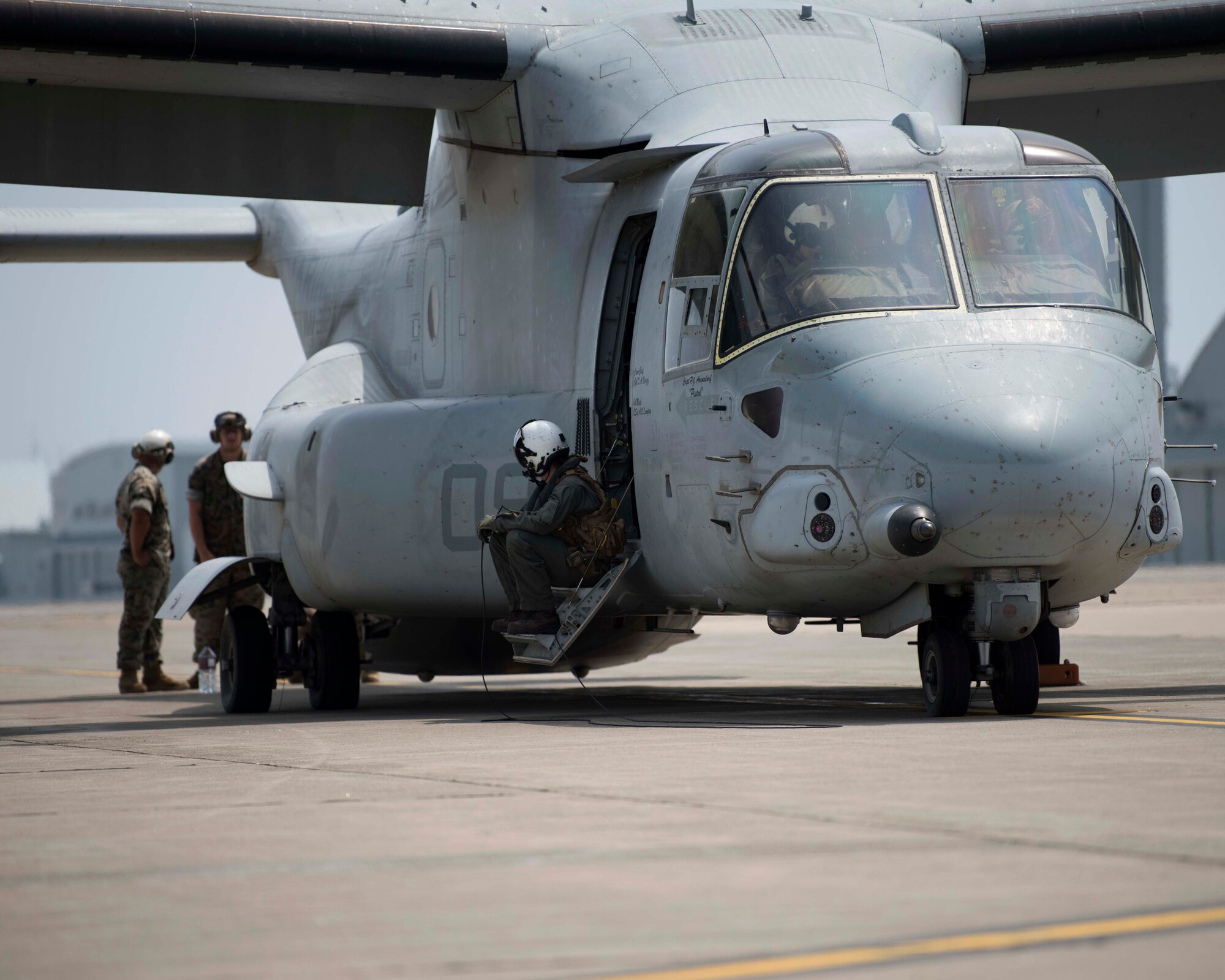 A grey aircraft sits on a flight line while individuals in flight suits operate it