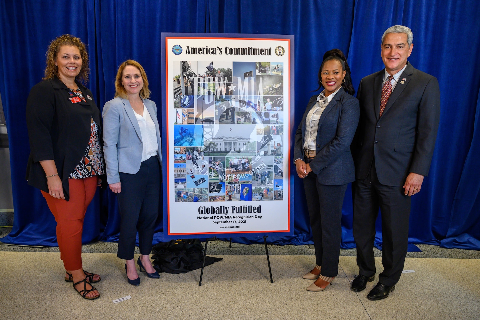 Deputy Defense Secretary Kathleen H. Hicks and other officials stand by a poster on display.