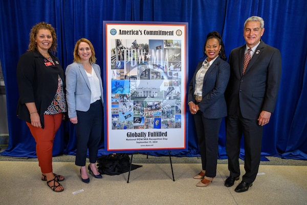 Deputy Defense Secretary Kathleen H. Hicks and other officials stand by a poster on display.