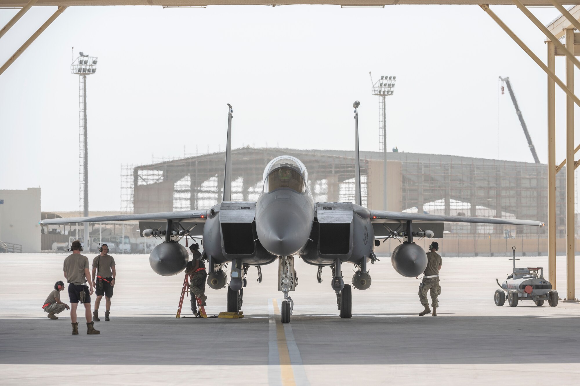 F-15E under a sunshade with maintenance Airmen working around it