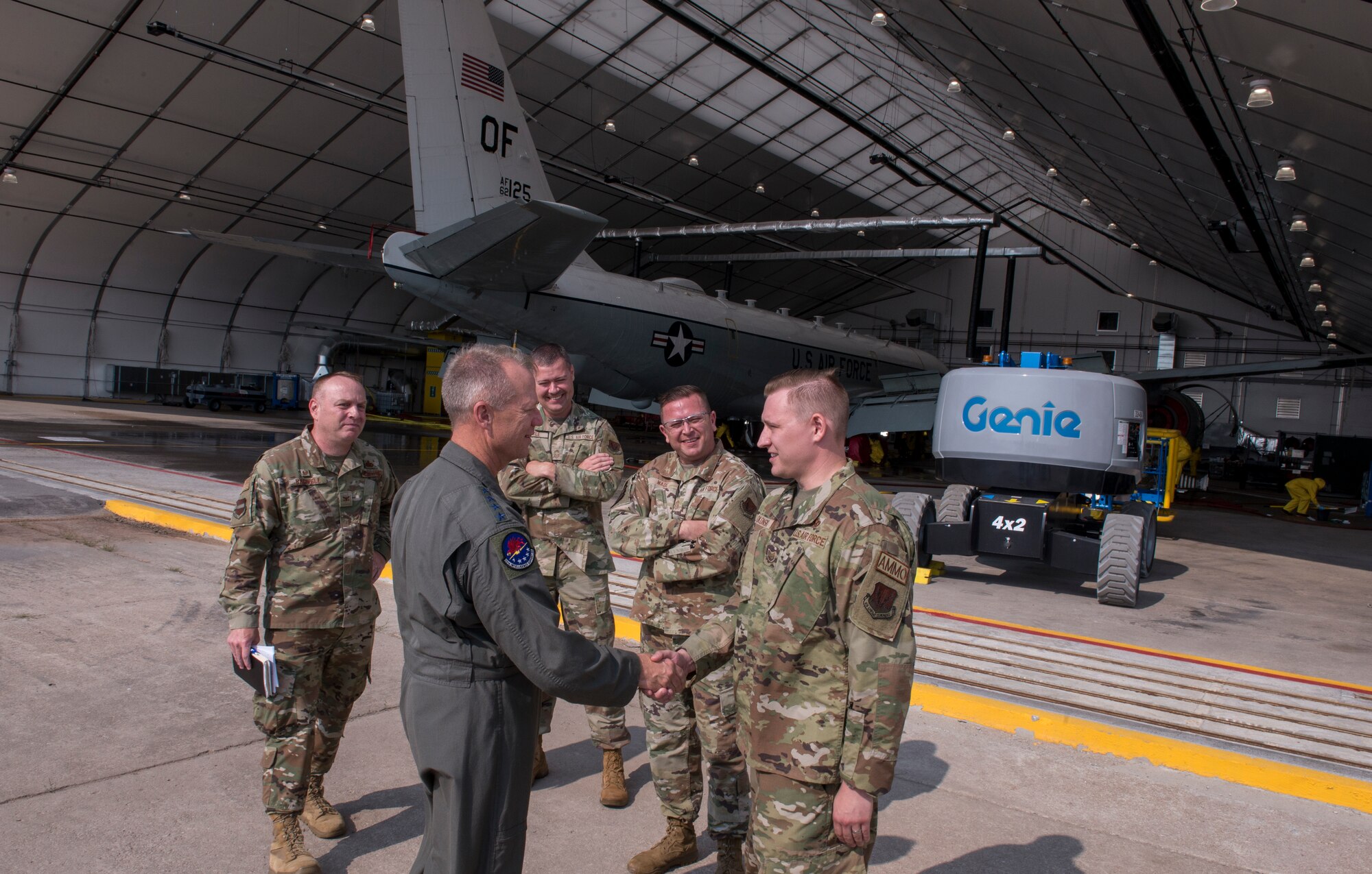 A group of uniformed Air Force Airmen talk and shake hands outside an aircraft hangar.