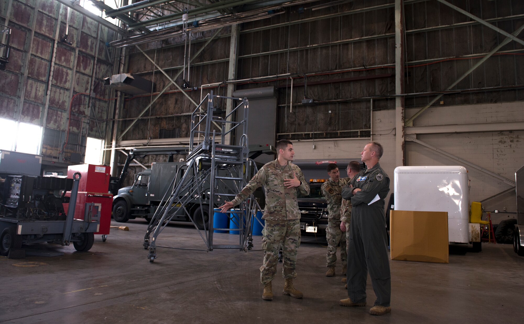 Two men in Air Force uniforms talk in an aircraft hangar.