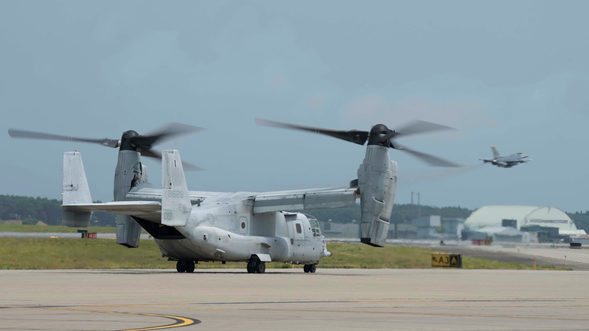 A grey aircraft sits on a flight line while individuals in flight suits operate it