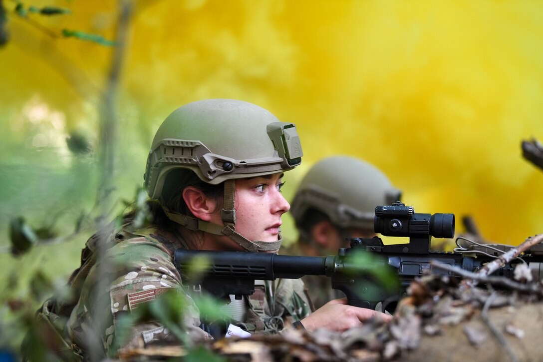 An airman holding a weapon lies on the ground and looks ahead.
