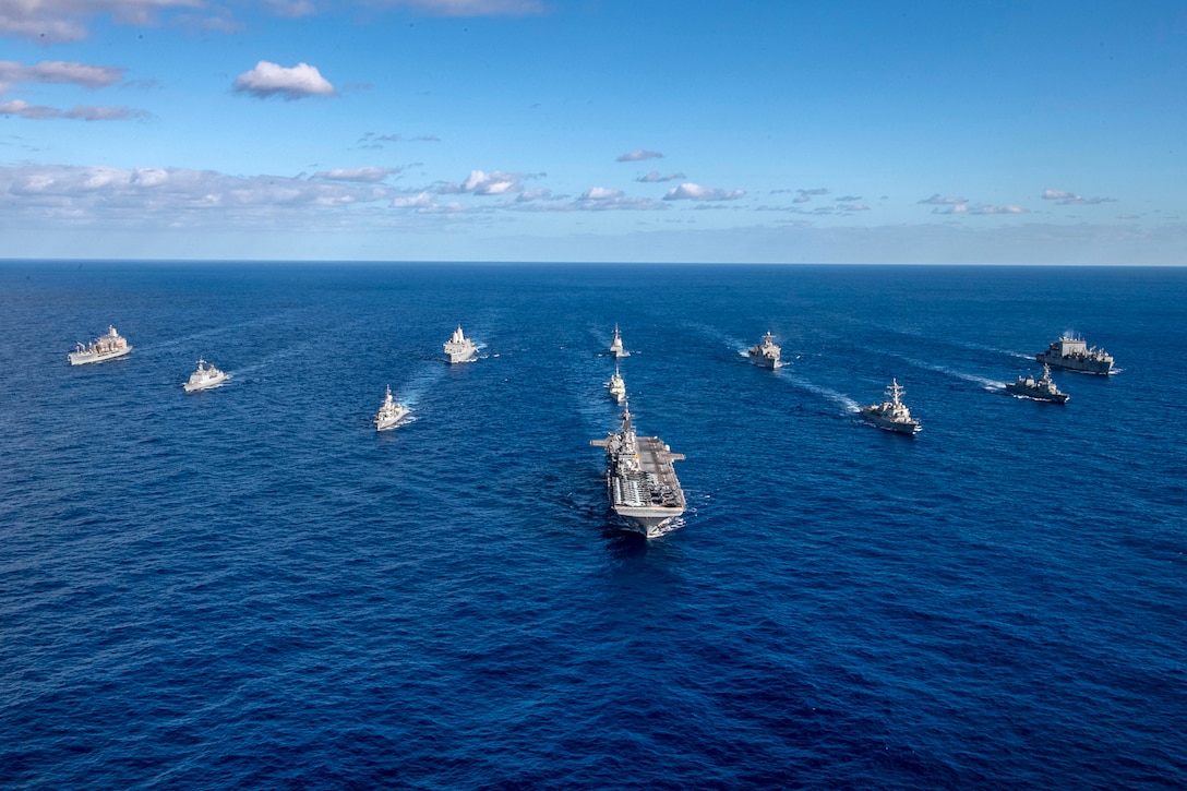 A group of ships steam in formation in the ocean.