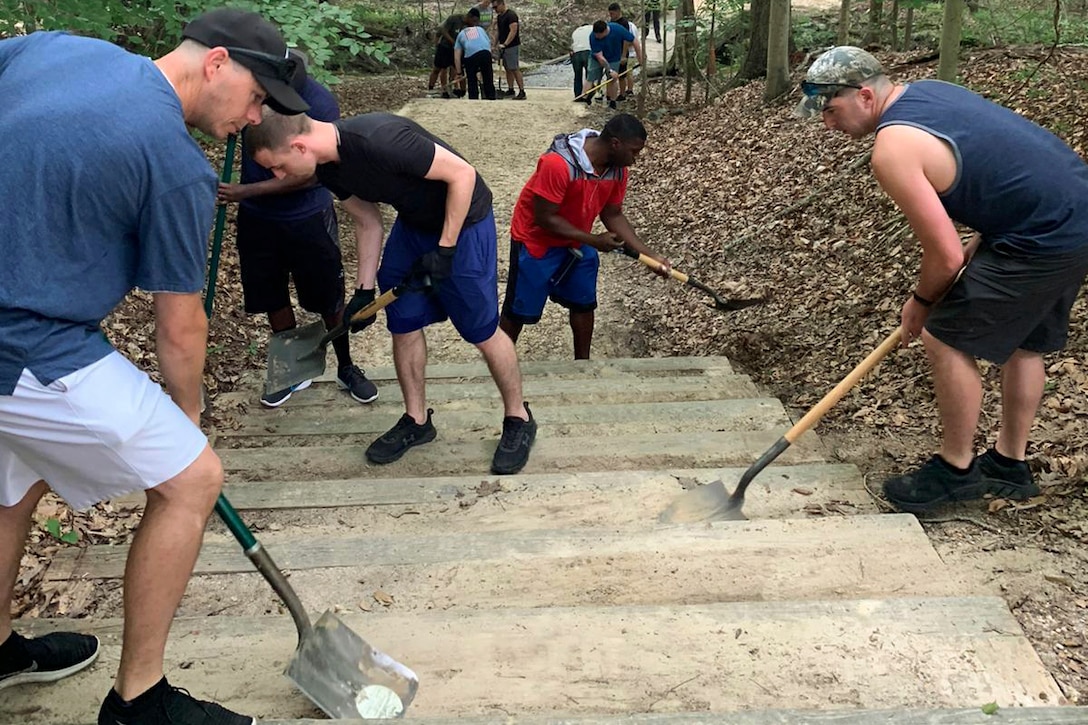 Soldiers clean a pathway in the woods.