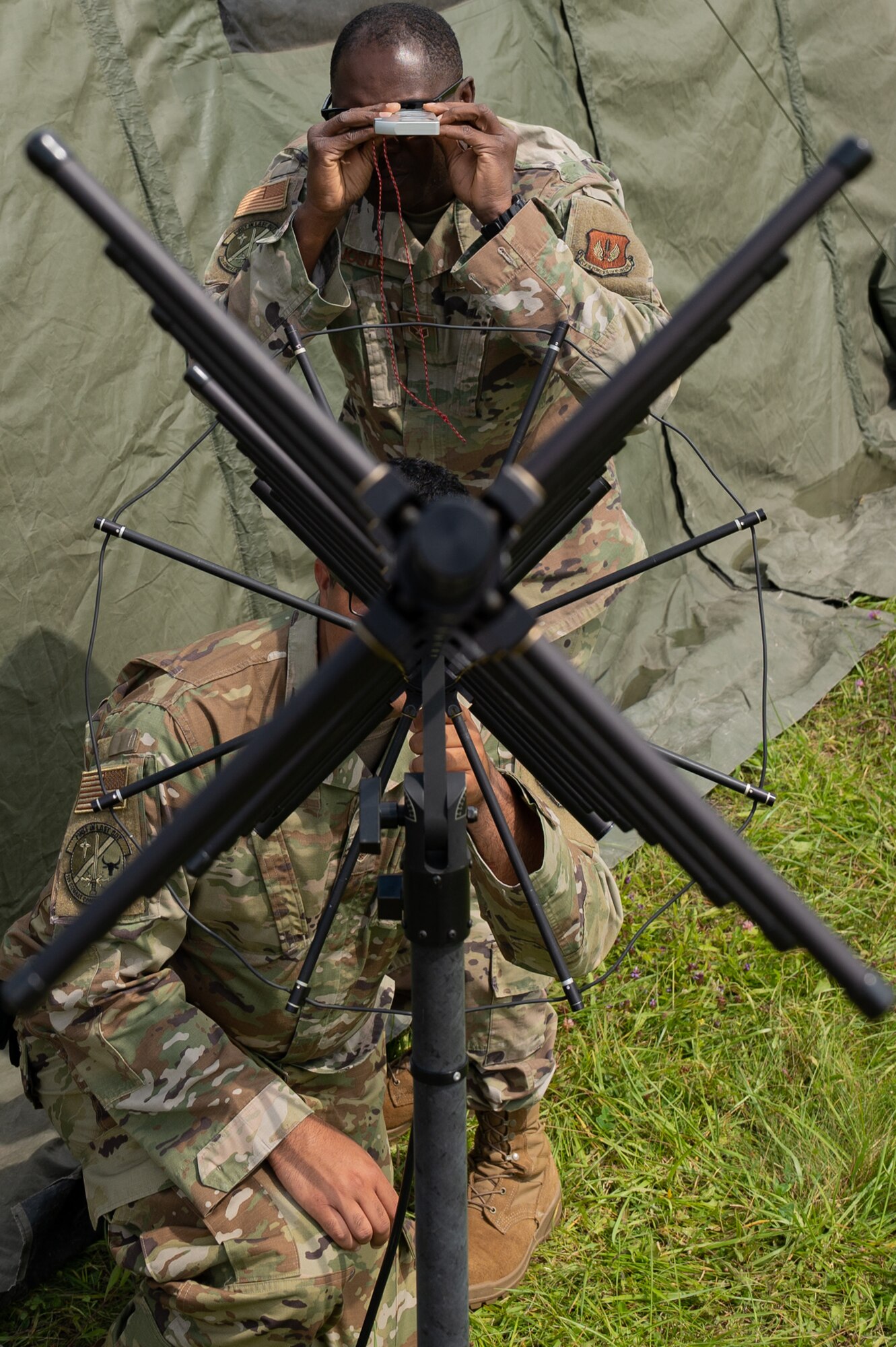 Two Airmen standing behind an antenna.