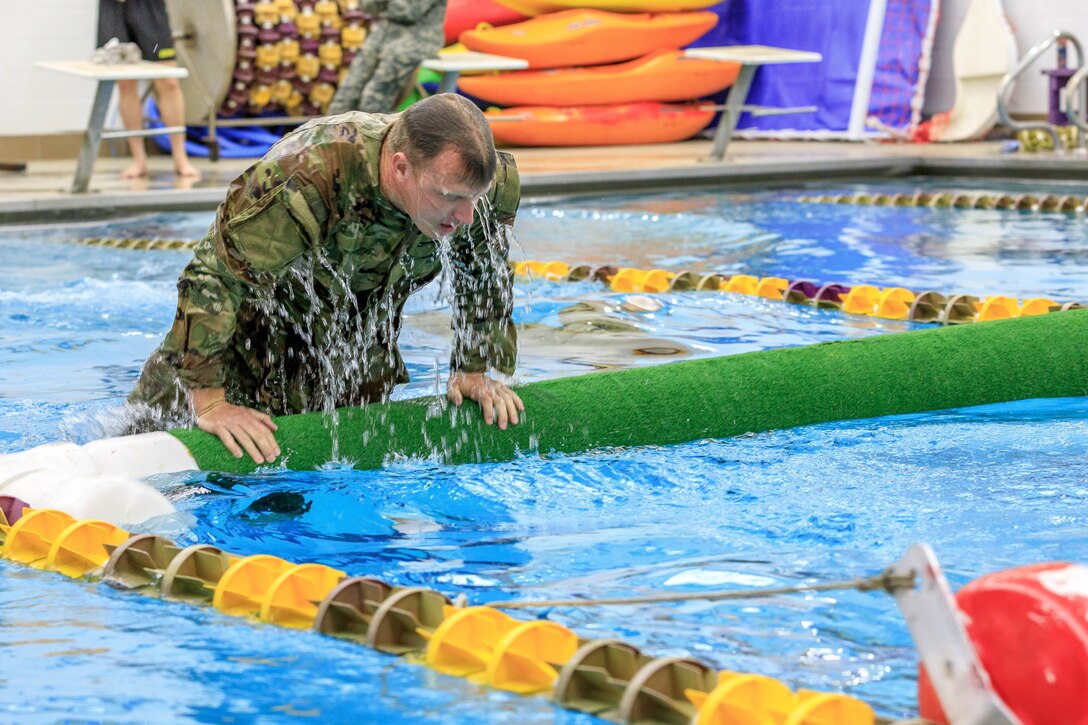 A soldier climbs over a tube in a swimming pool.