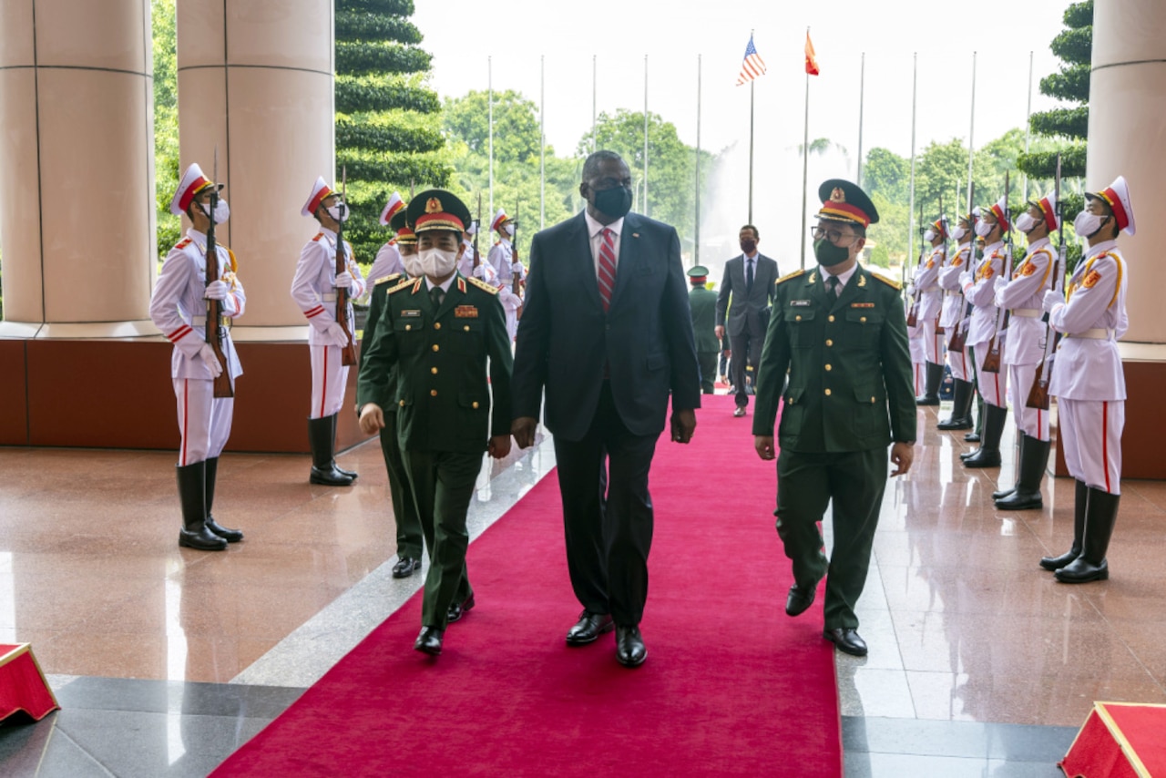 The U.S. Defense Secretary walks on a red carpet with Vietnamese military officials.