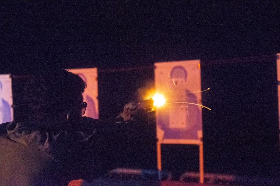 A Marine fires a weapon at a target illuminated by an orange light.