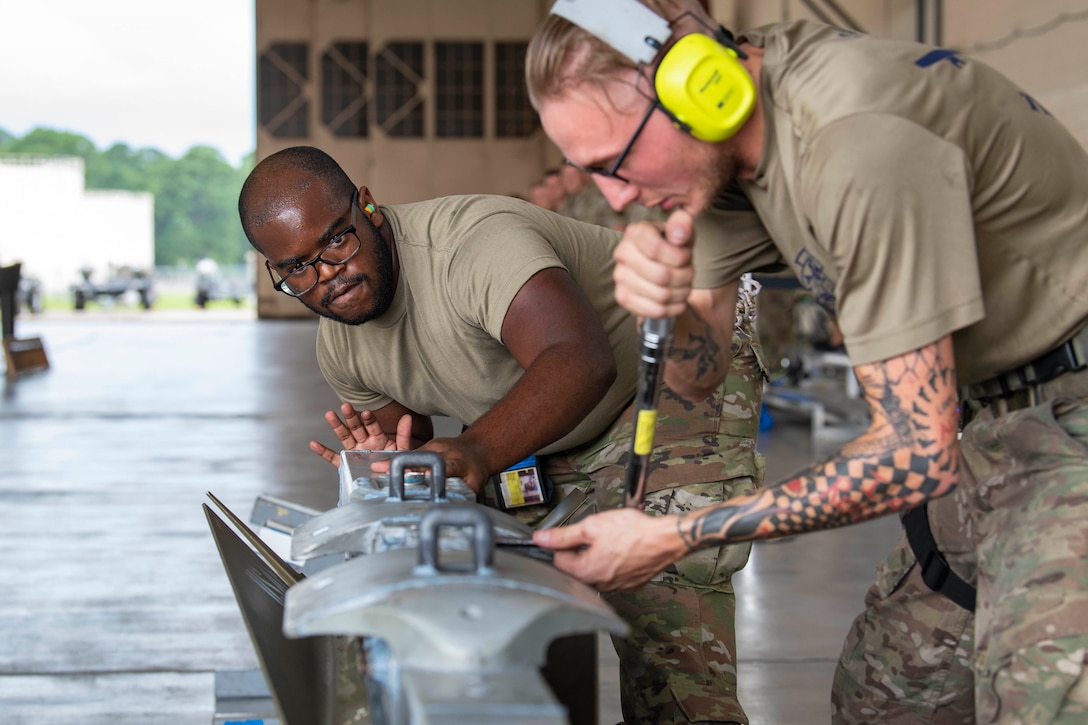 Two airmen work on a weapon in a garage-like area.