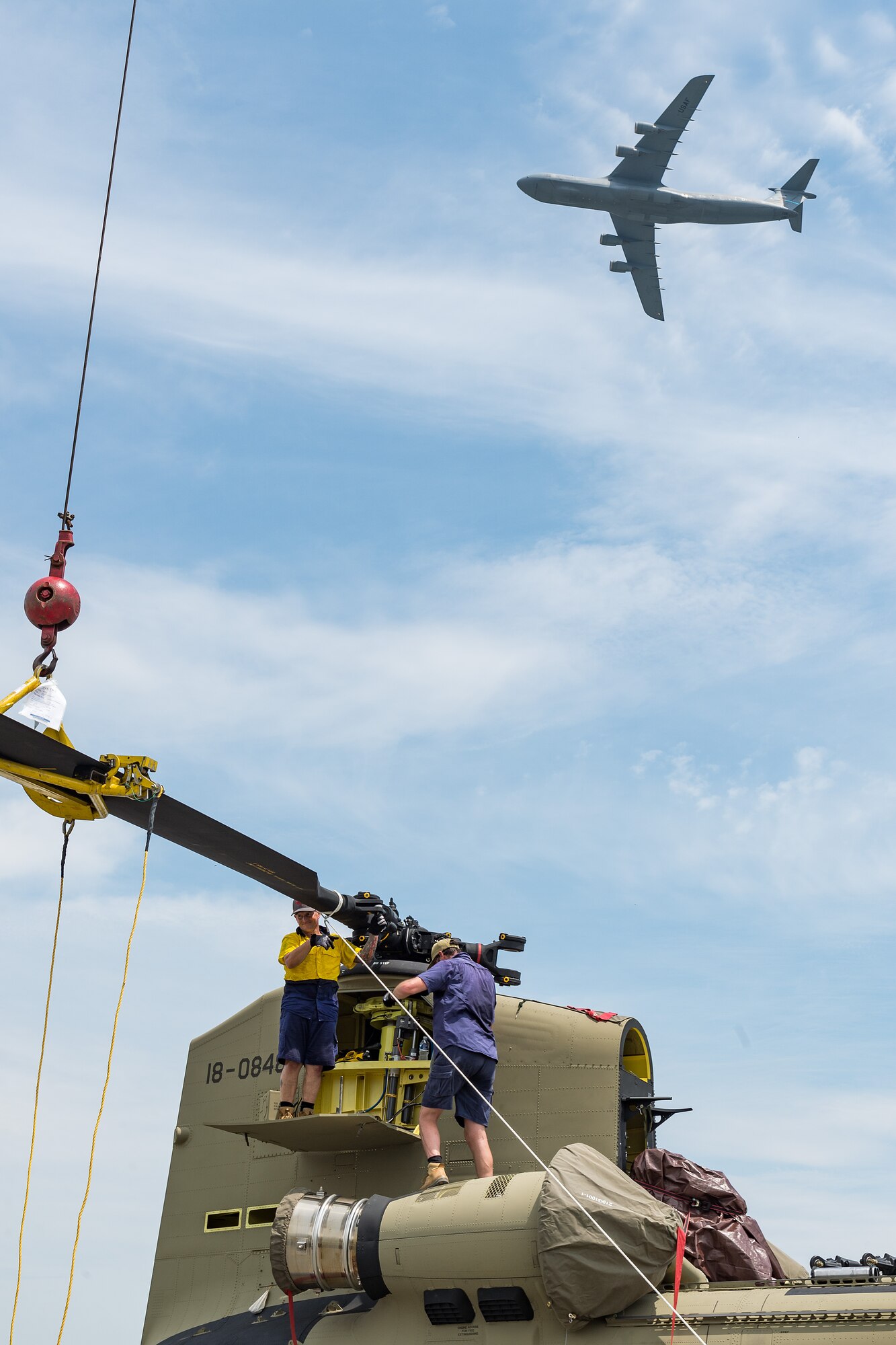 Boeing Defence Australia maintenance team members remove a rotor blade from a CH-47F Chinook helicopter as a C-5M Super Galaxy flies overhead at Dover Air Force Base, Delaware, June 9, 2021. BDA maintenance personnel readied two Chinooks for shipment aboard a C-5M Super Galaxy as part of the U.S. government’s foreign military sales program. The U.S.-Australia alliance is an anchor for peace and stability in the Indo-Pacific region and around the world. (U.S. Air Force photo by Roland Balik)
