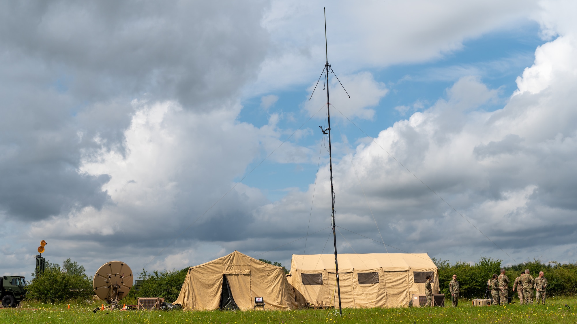 A distant view of Airmen standing next to tents and antenna.