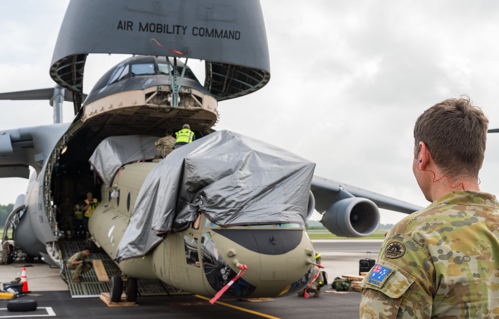 A member of the Australian Army observes the winching-in of a  CH-47F Chinook helicopter on the forward ramp of a C-5M Super Galaxy at Dover Air Force Base, Delaware, June 26, 2021. Boeing maintenance team members, 9th Airlift Squadron loadmasters and 436th Aerial Port Squadron ramp services personnel uploaded two Chinooks onto the aircraft as part of the U.S. government’s foreign military sales program. The U.S.-Australia alliance is an anchor for peace and stability in the Indo-Pacific region and around the world. (U.S. Air Force photo by Roland Balik)