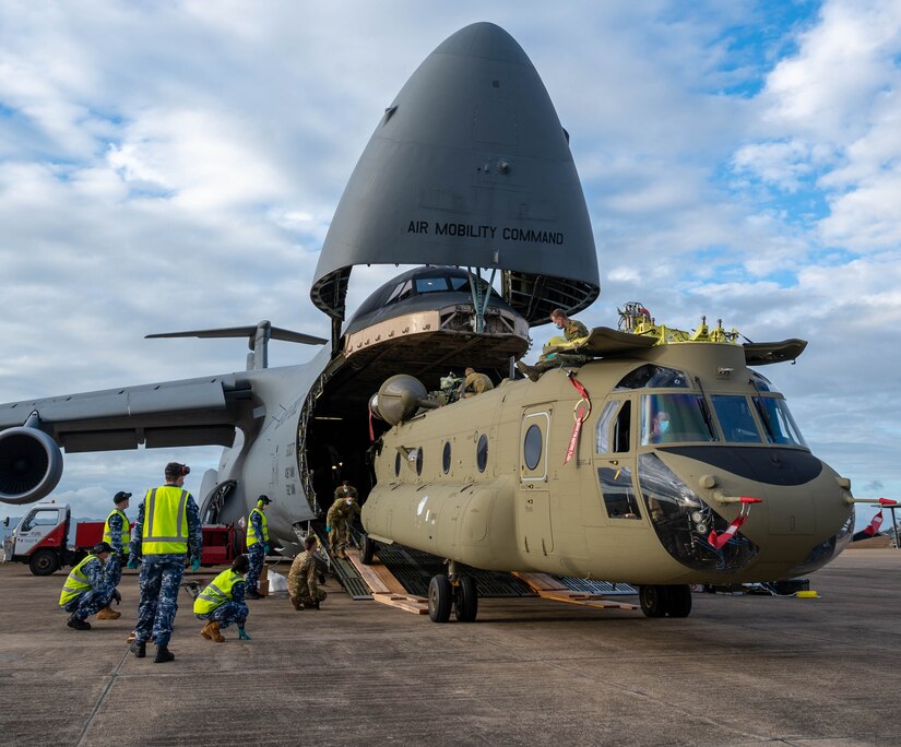 A helicopter is unloaded from the back of a large aircraft.