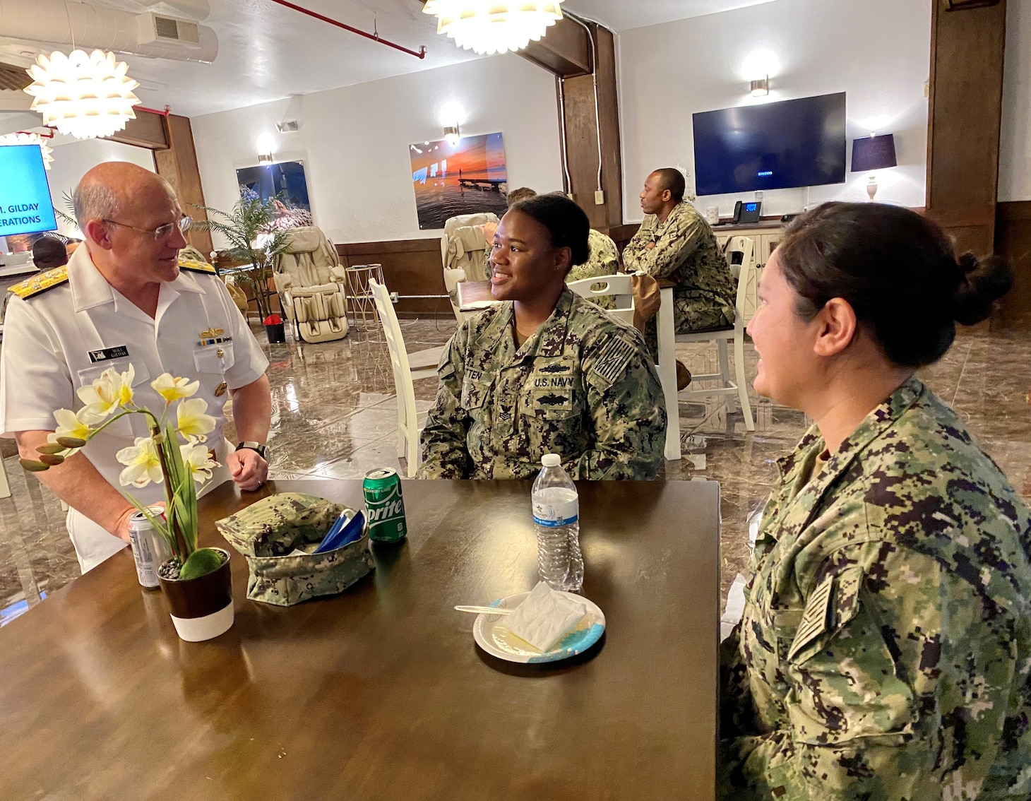 CNO Gilday speaks with two Sailors at a table.