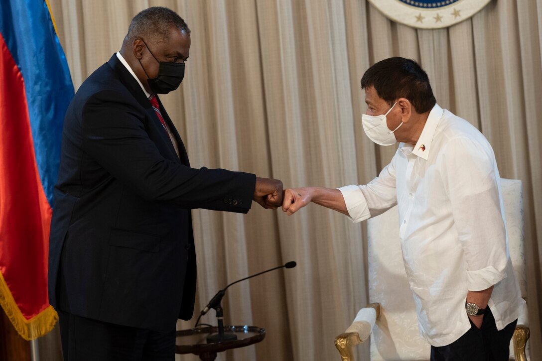 Two men do a fist bump handshake.