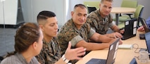 Three Marines and a civilian work in an open workspace environment