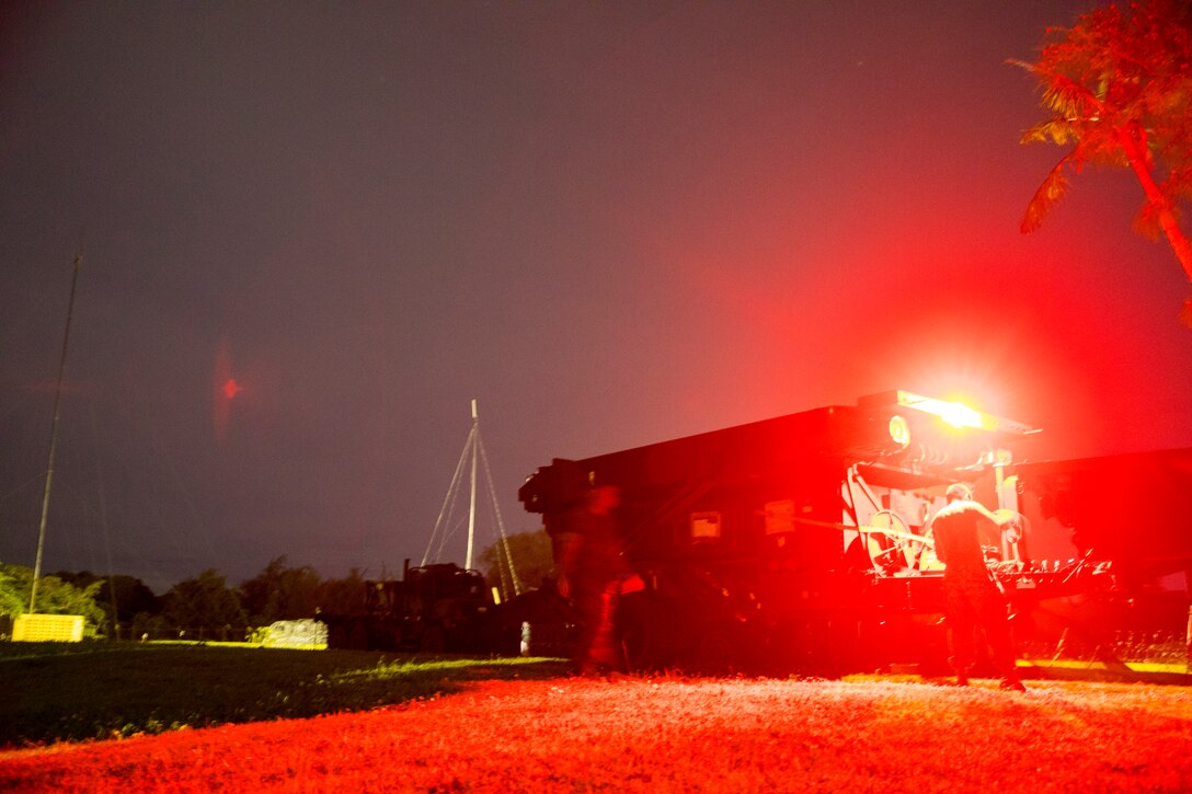 Marines set up a radar in field in the dark illuminated by red light.