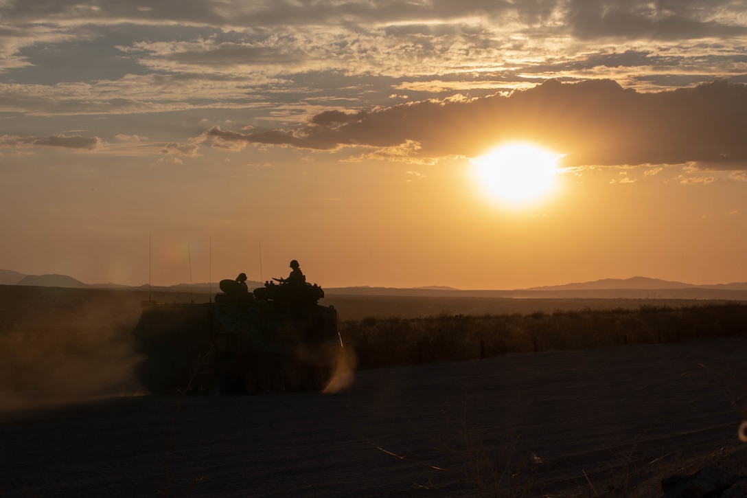 Marines ride in a tank in the desert at twilight.