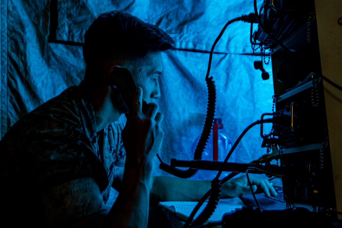 A Marine illuminated by blue light talks into a phone.