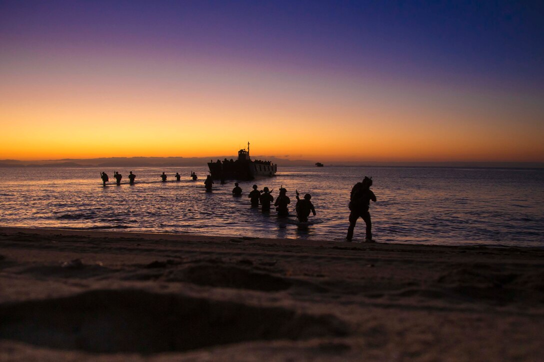 Marines walk onto a beach from an amphibious vehicle.