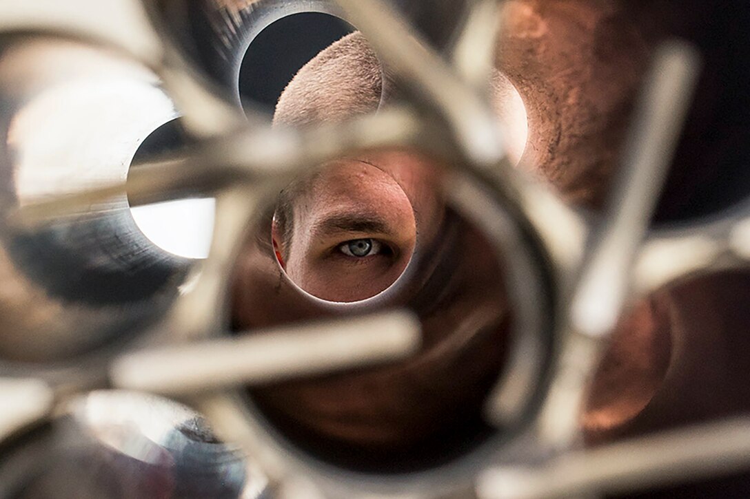 A Marine's eye is visible as he looks into an opening of a metallic helicopter part.