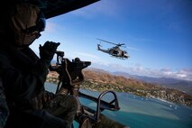 A U.S. Marine Corps crew chief with Marine Light Attack Helicopter Squadron 367 waves at a fellow UH-1Y Venom utility helicopter during an Intrepid Tiger II exercise, Marine Corps Training Area Bellows, Oahu, July 22, 2021. The Intrepid Tiger II Electronic Warfare capability embodies Marine Corps Base Hawaii’s goal to modernize resources to provide the tools required to ensure the readiness of the individual warfighter. (U.S. Marine Corps photo by Lance Cpl. Samantha Sanchez)