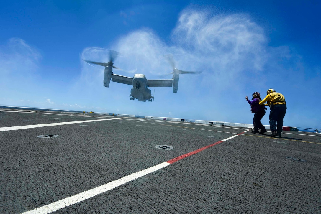 One of two sailors signals a hovering helicopter from the deck of a ship.