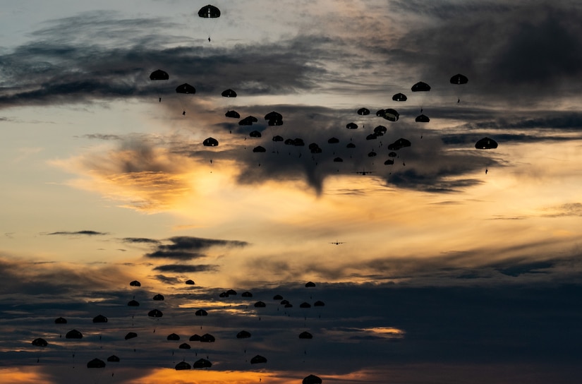 Parachutes descend in a pink- and blue-streaked sky.