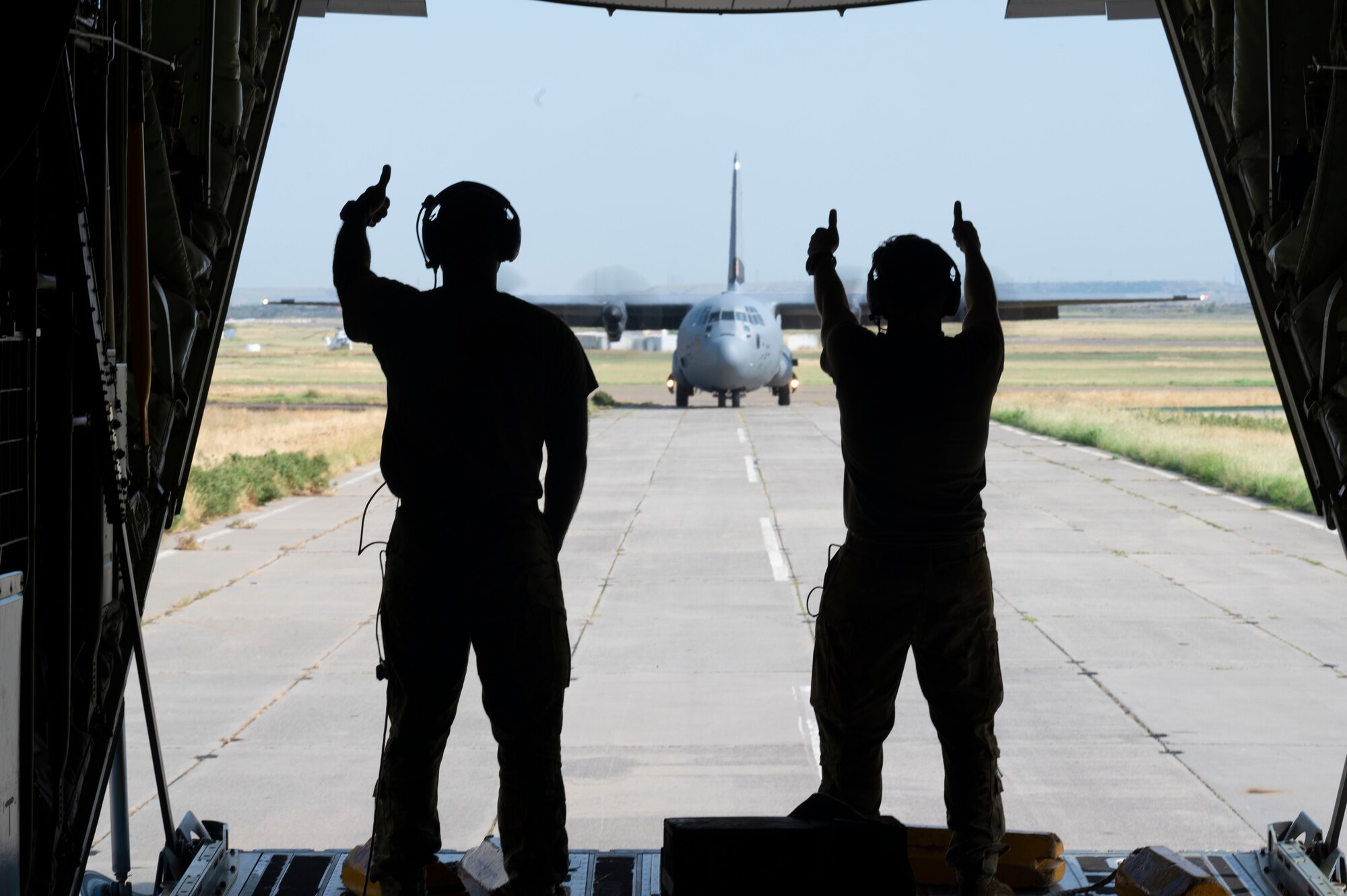 U.S. Air Force Tech. Sgt. Mario Linton, 37th Airlift Squadron loadmaster, left, and Senior Airman Robert Kucholtz, 37th AS loadmaster, give a thumbs up to the 37th AS pilots of a U.S. Air Force C-130J Super Hercules aircraft during exercise Agile Spirit 21