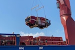A large item is hoisted onto a ship.