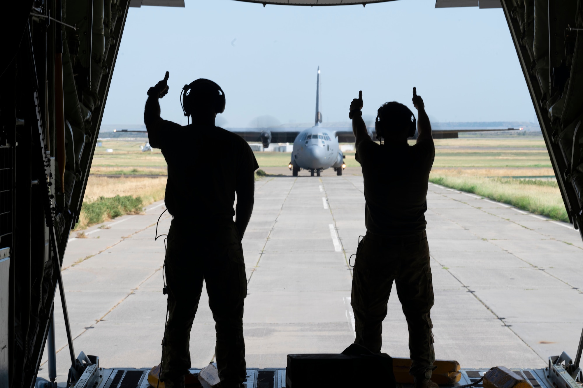 U.S. Air Force Tech. Sgt. Mario Linton, 37th Airlift Squadron loadmaster, left, and Senior Airman Robert Kucholtz, 37th AS loadmaster, give a thumbs up to the 37th AS pilots of a U.S. Air Force C-130J Super Hercules aircraft during exercise Agile Spirit 21.