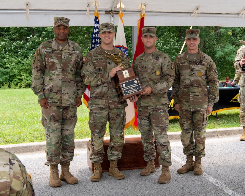 four men and women in army uniforms standing in front of flags.