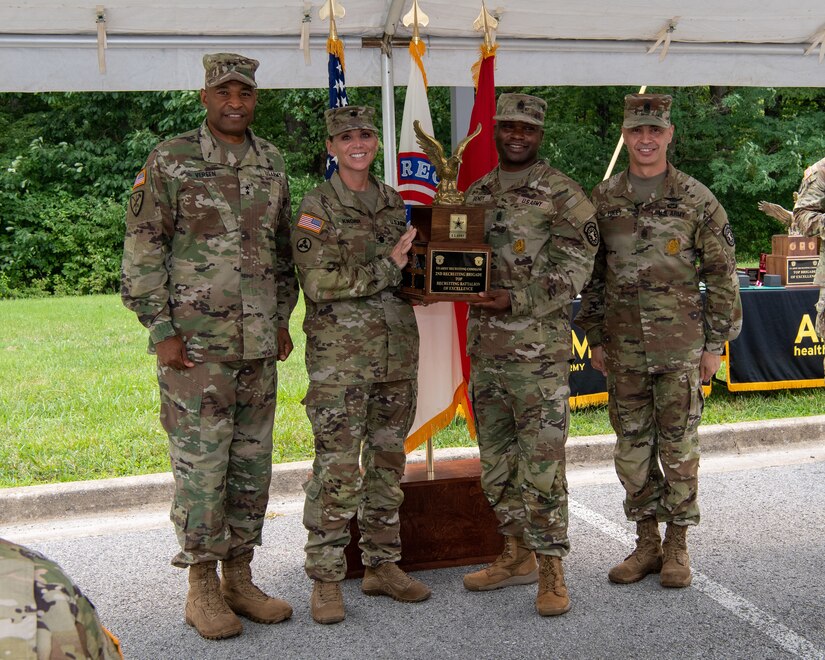 four men and women in army uniforms standing in front of flags.