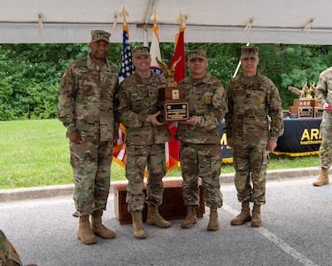 four men in army uniforms standing in front of flags.