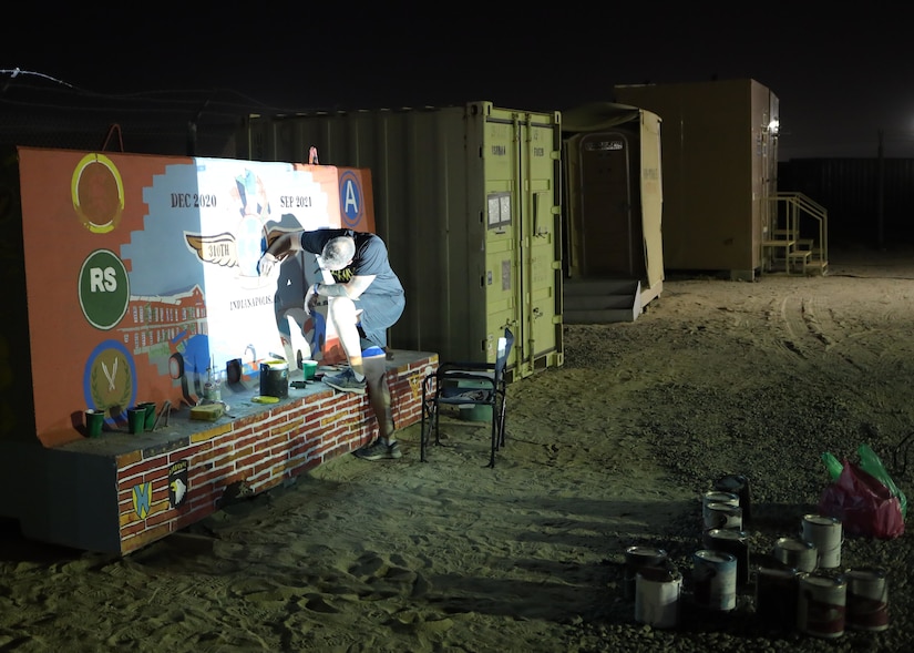 Chief Warrant Officer 2 Paul Viall, information systems technician, assigned to the 310th Sustainment Command (Expeditionary), works at night with the aid of a projector to trace out the design of the unit mural or unit T-wall, Camp Arifjan, Kuwait.  Viall worked countless hours to paint a mural that will represent the hard work and dedication of the Army Reserve’s Indianapolis-based “Brickyard” Soldiers and their time serving within the U.S. Central Command’s area of responsibility.