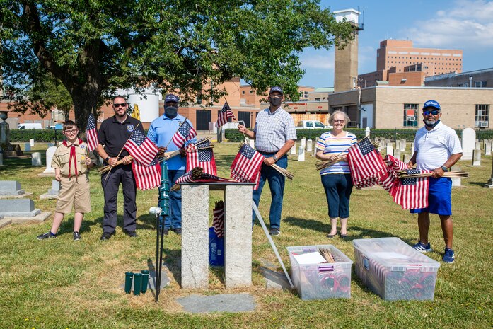 Norfolk Naval Shipyard employees joined members of Naval Support Activity Hampton Roads Portsmouth as well as members of the Portsmouth Chapter of the Navy Wives Club at the Captain Ted Conaway Memorial Naval Cemetery in Naval Medical Center Portsmouth (NMCP) May 27 for their annual flag placement ceremony in honor of Memorial Day, placing more than 880 flags on the graves of fallen service members from eight countries.