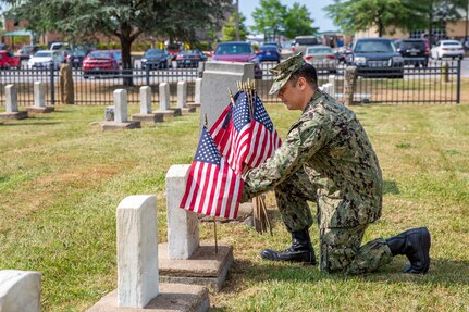 A Sailor stationed at Naval Support Activity Hampton Roads Portsmouth places flags on the graves of fallen service members during the annual flag placement ceremony at the Captain Ted Conaway Memorial Naval Cemetery in Naval Medical Center Portsmouth (NMCP) May 27.