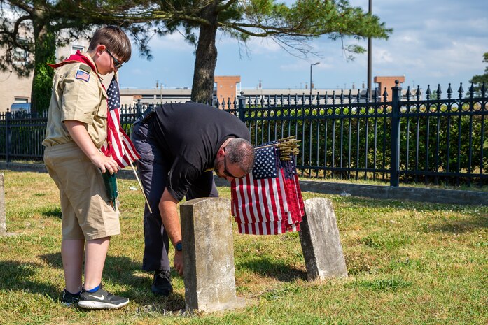 Norfolk Naval Shipyard Veteran Employee Readiness Group President Nicholas Boyle and his son Connor Boyle place flags on the graves of fallen service members during the annual flag placement ceremony at the Captain Ted Conaway Memorial Naval Cemetery in Naval Medical Center Portsmouth (NMCP) May 27.