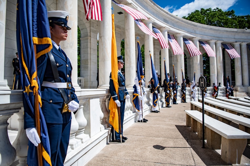 Service members stand at attention in an amphitheater.