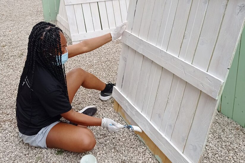 A woman sits on the ground painting a board.