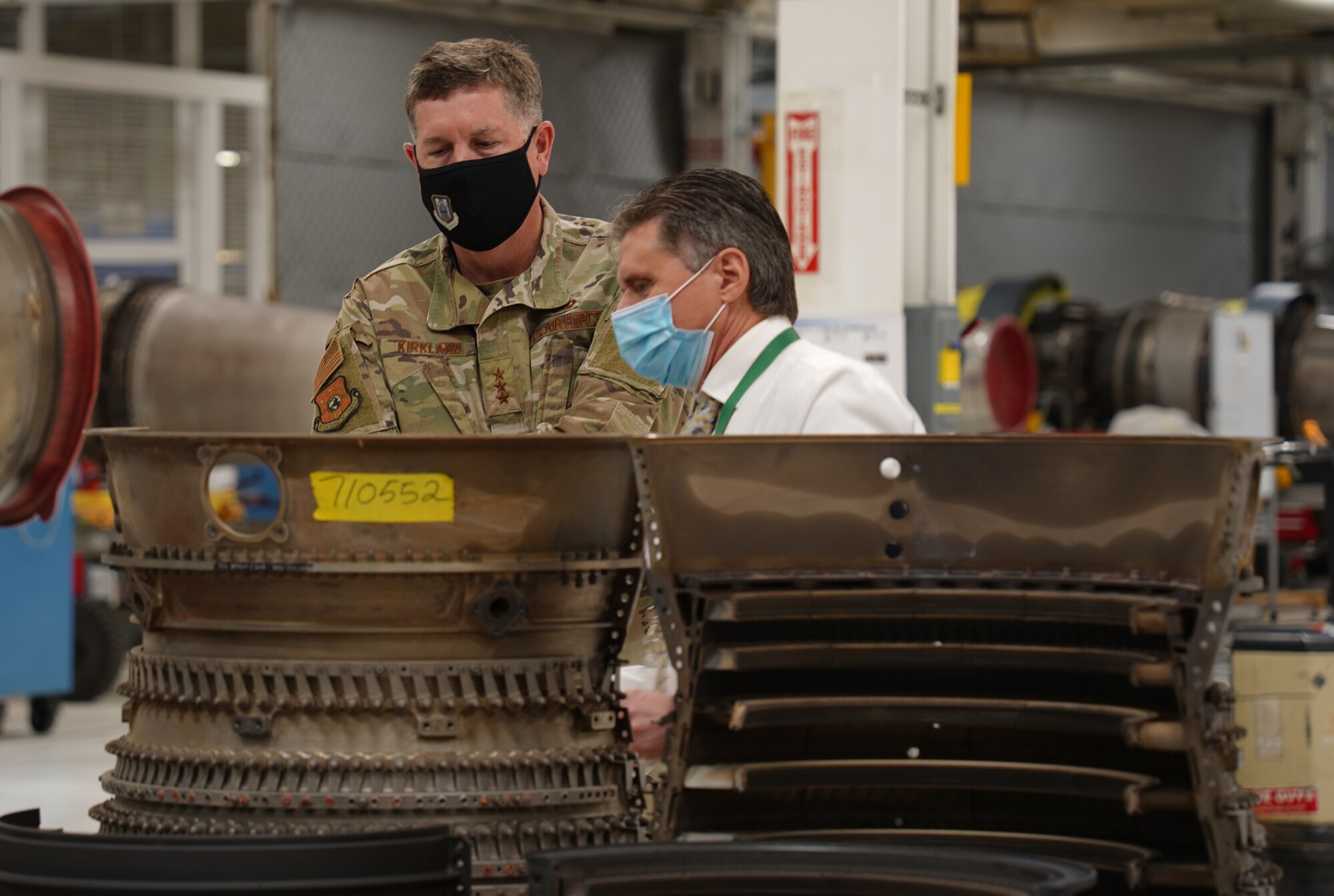 Two men with an aircraft engine part in front of them.