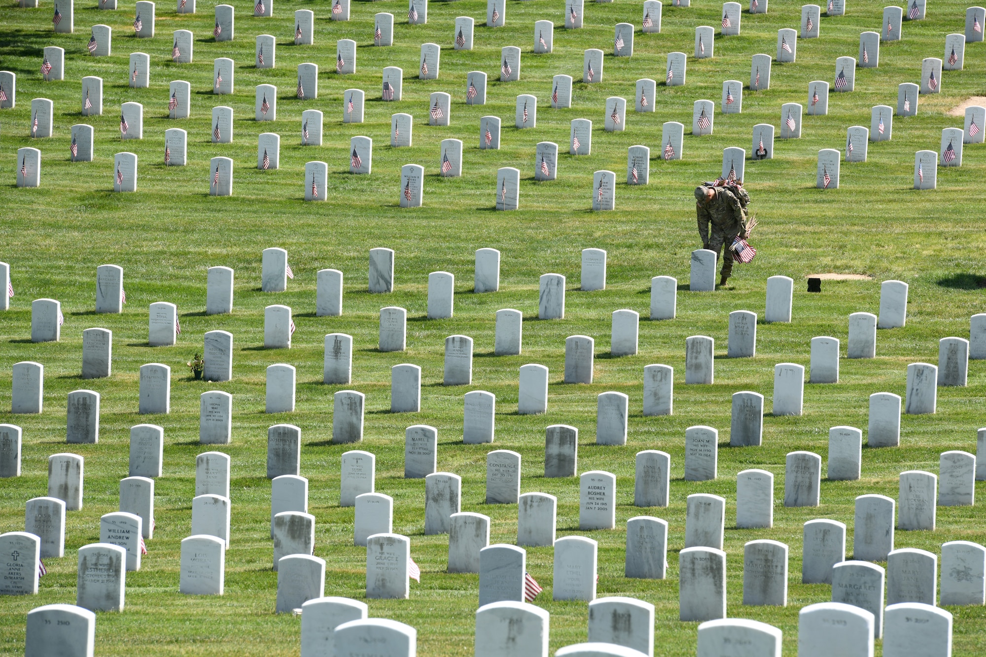 Man in uniform placing flag in front of headstone.