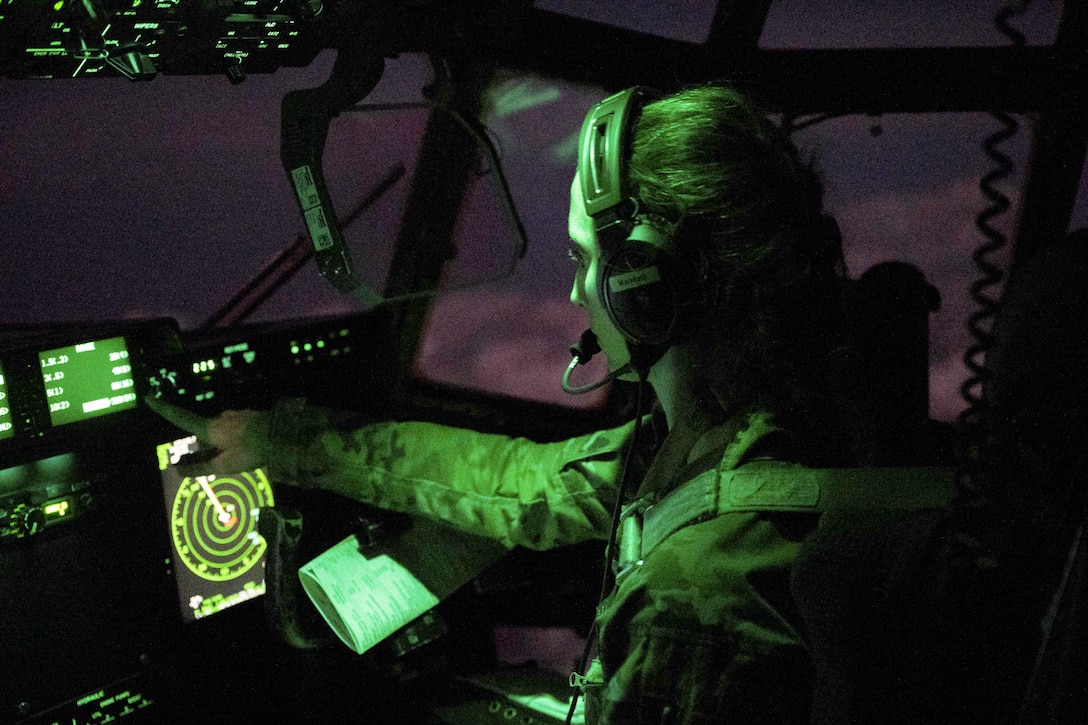 An airmen sits in the cockpit illuminated by green lights.