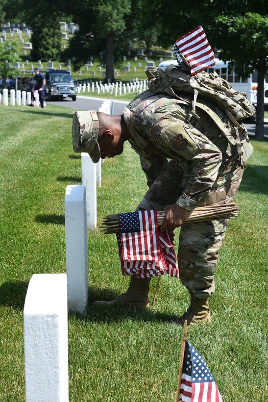 Man in uniform placing flag in front of headstone.