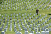 Man in uniform placing flag in front of headstone.