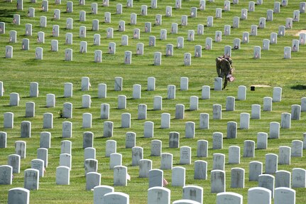 Man in uniform placing flag in front of headstone.